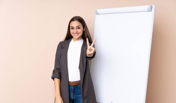 Young woman giving a presentation on white board smiling and showing victory sign - Valokuva, kuva