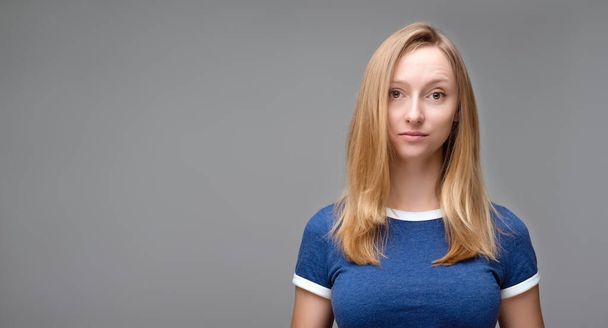 Retrato de una joven hermosa mujer con cabello rubio y camiseta azul mirar a la cámara, posando en el estudio, aislado sobre fondo gris estudio. Copia espacio para tu texto - Foto, Imagen