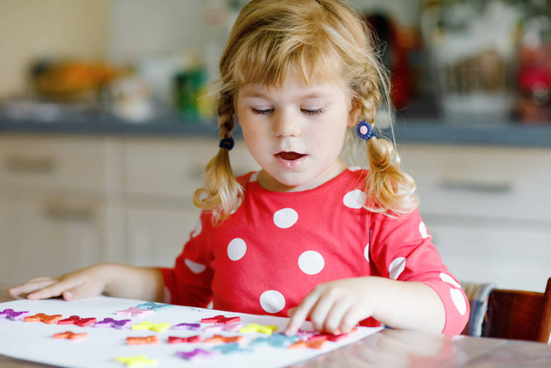 Mała dziewczynka maluch bawi się z różnych kolorowych naklejek i malowanie kwiatów. Koncepcja aktywności dzieci podczas pandemicznej kwarantanny wirusa korony. Dziecko uczy się kolorów z rodzicami w domu - Zdjęcie, obraz