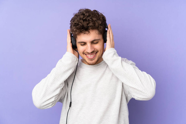 Caucasian man isolated on purple background listening music - Foto, imagen