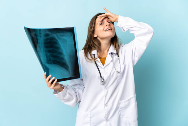 Молода лікарка, що тримає рентгенографію над ізольованим тлом, робить несподіваний жест, дивлячись на бік
 - Фото, зображення