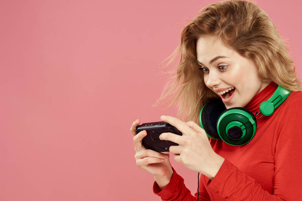 Woman with mobile set-top box headphones playing lifestyle pink background red jacket - Zdjęcie, obraz