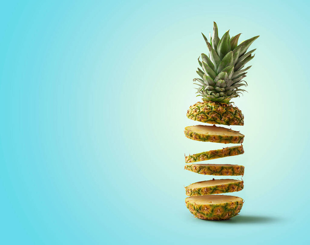 Fresh pineapple cut into slices flying, isolated from the blue background with copy space - Valokuva, kuva