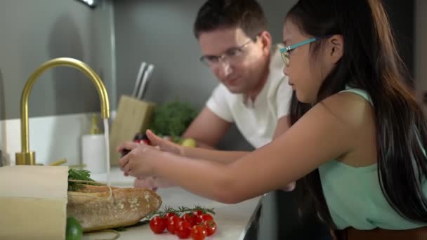 Ο όμορφος λευκός πατέρας και η κόρη του πλένουν φρούτα στον νεροχύτη της κουζίνας κατά τη διάρκεια της πανδημίας.  - Πλάνα, βίντεο