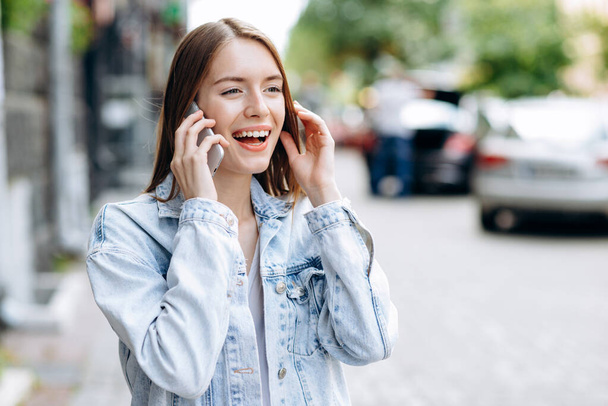 Smiling, cheerful girl outdoors talking on the phone - Fotó, kép
