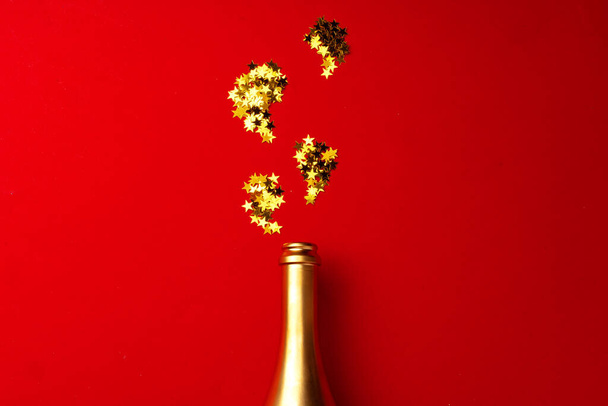Champagne bottle with sparkling confetti on red background flat lay - Photo, Image