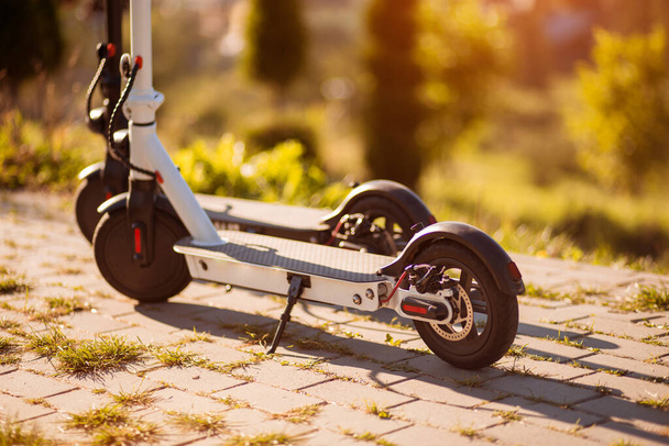 Sonbaharda gün batımında şehir şehrini keşfetmeye hazır iki modern elektrikli scooter. Ekolojik şehir taşımacılığı kavramı - Fotoğraf, Görsel