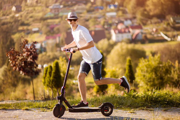 Joven empresario con scooter eléctrico se apresura a trabajar en el parque de otoño - Foto, imagen