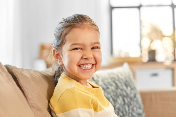 happy smiling little girl sitting on sofa at home - Valokuva, kuva