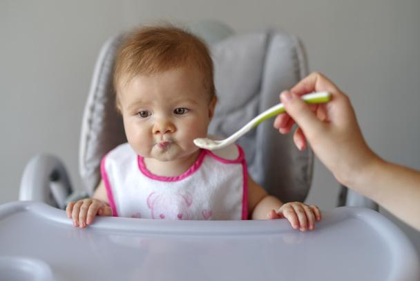 Mother feeding baby daughter with spoon in high chair - Photo, Image