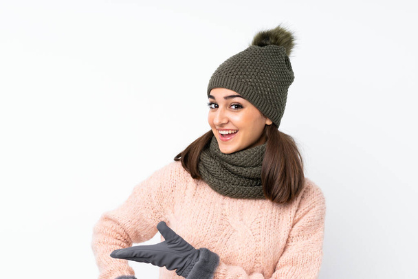 Молодая девушка в зимней шляпе на изолированном белом фоне протягивая руки в сторону для приглашения прийти - Фото, изображение