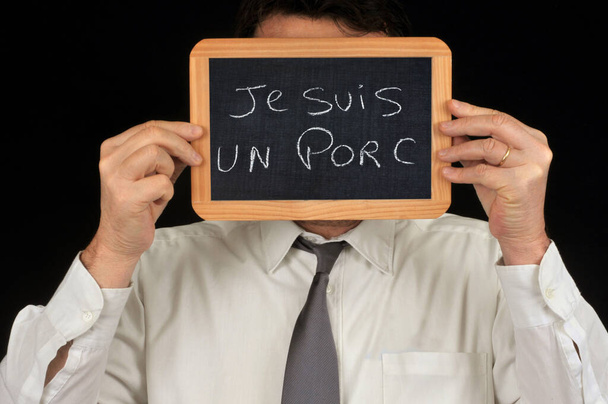 フランス語で書かれている学校のスレートで顔を隠す匿名の男私は豚です  - 写真・画像