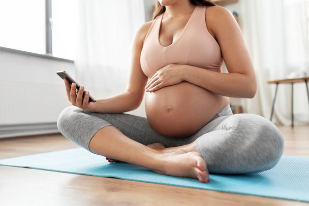 happy pregnant woman with phone doing yoga at home - Valokuva, kuva