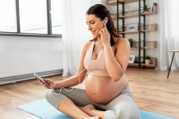 pregnant woman with earphones doing yoga at home - Фото, изображение