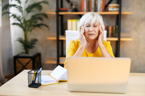 Tired senior business woman is using laptop - Фото, изображение
