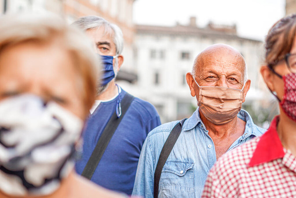Şehir sokaklarında maskeli yaşlı bir adama odaklanan bir grup insan, yeni bir yaşam tarzına odaklanıyor. - Fotoğraf, Görsel