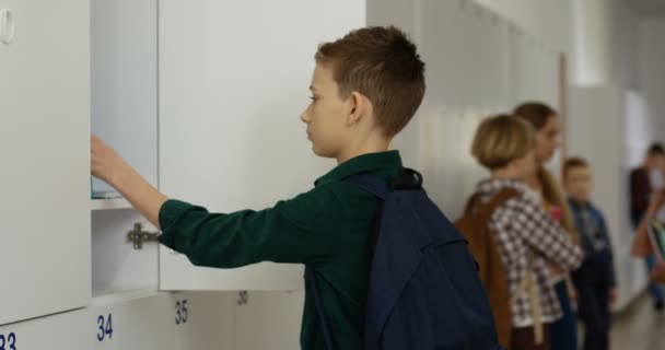 Caucasian teen scholboy taking out textbooks from his locker and then smiling to the camera at the school corridor. Portrait shot. - Footage, Video