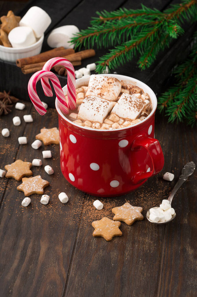 Big red Cup hot Chocolate drink with Marshmallows, gingerbread cookies, candy cane and cinnamon on dark wooden background. Winter time. Holiday concept, Selective focus - Foto, Imagem