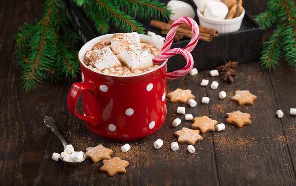 Große rote Tasse heißes Schokoladengetränk mit Marshmallows, Lebkuchen, Zuckerrohr und Zimt auf dunklem Holzgrund. Winterzeit. Urlaubskonzept, selektiver Fokus - Foto, Bild