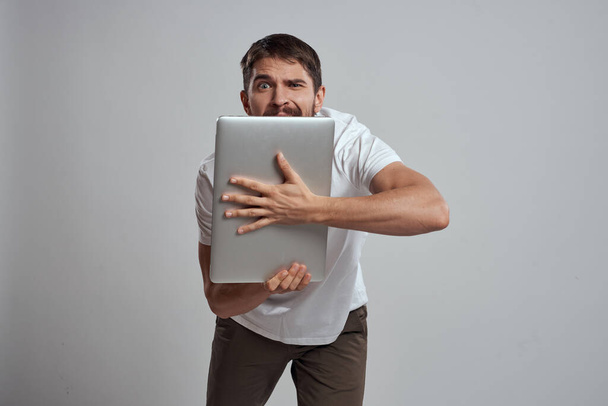 Un hombre con un portátil en sus manos sobre un fondo claro en una camiseta blanca emociones fondo claro nuevas tecnologías - Foto, imagen