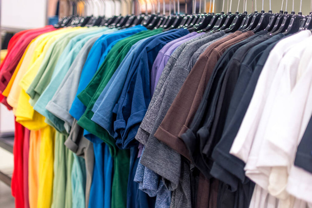 Una selección de camisetas de varios colores que se muestran en un estante de ropa en una tienda departamental. - Foto, imagen