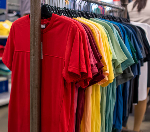 Una selección de camisetas de varios colores que se muestran en un estante de ropa en una tienda departamental. - Foto, imagen