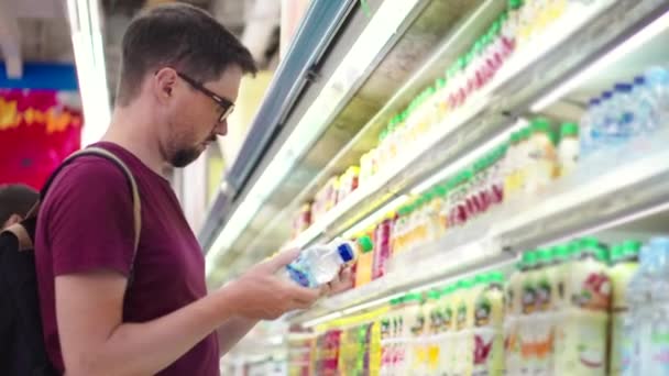 Jeune homme achète de l'eau et du jus dans un supermarché - Séquence, vidéo