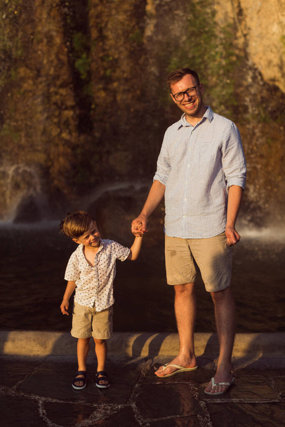 The happy young dad is standing with his little son on the rock background - Fotoğraf, Görsel