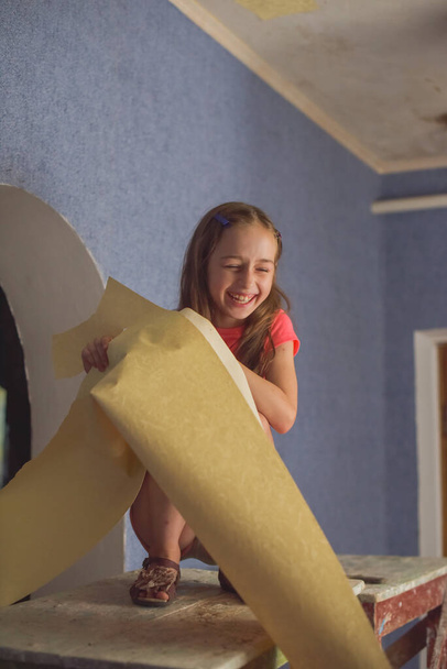 A lány leveszi a régi tapétákat a falról. A lány segít ragasztani a tapétát. Egy tinédzser segít a szüleinek. Lakásfelújítási koncepció. - Fotó, kép