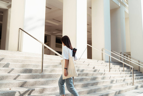 Симпатичная девушка в белой футболке поднимается по лестнице здания под солнцем. - Фото, изображение