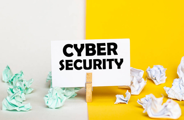 bílý papír s textem Kybernetická bezpečnost na kolíku na žlutém a bílém pozadí s papírovými balíky různých barev - Fotografie, Obrázek