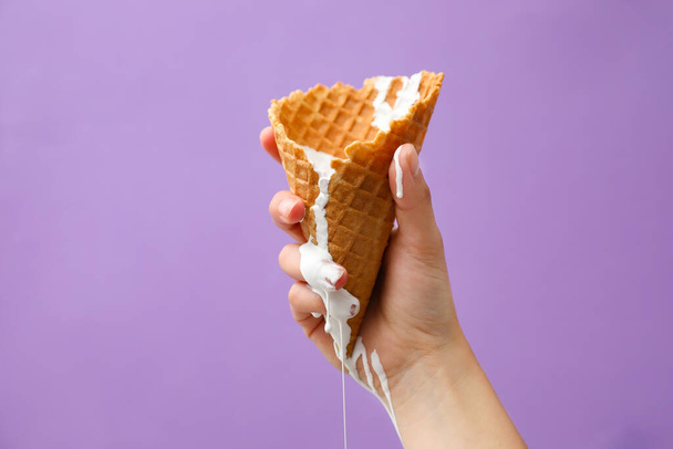 Woman holding wafer cone with molten ice cream on violet background, closeup - Photo, Image