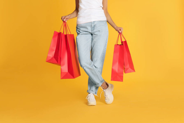 Young woman with paper shopping bags on yellow background, closeup - Foto, afbeelding