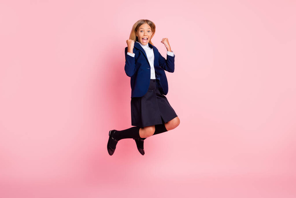 Photo of cute pretty small lady excited jumping fists up scream yeah win history quiz first place class wear uniform blue jacket shirt skirt black stockings isolated pink color background - Foto, Bild