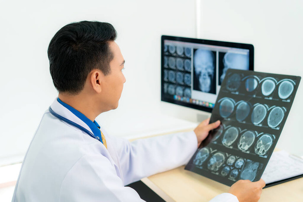 Asiático hombre médico celebración y mirando a examinar la radiografía de los pacientes cráneo y cerebro en una clínica médica en el hospital.  - Foto, imagen
