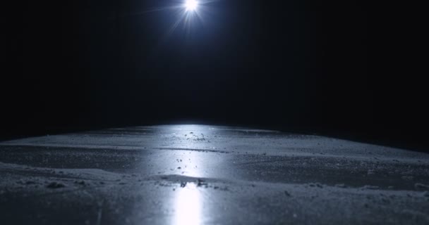 Close-up van voeten van haveloze speler of schaatser op schaatsers glijden op ijzige ondergrond in het donker. Schaatsen op de ijsbaan in het licht van een enkele spotlamp. Hockey-wedstrijdconcept. - Video