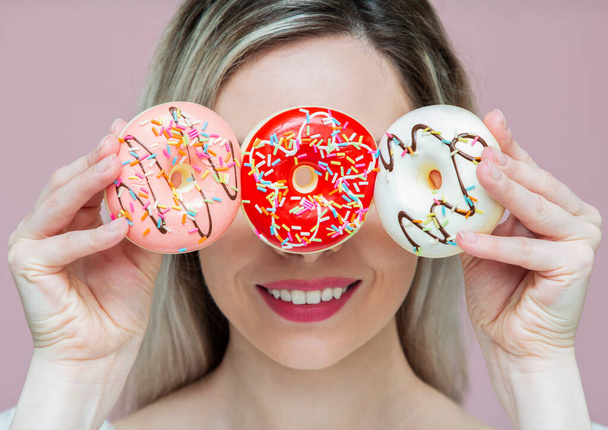 beautiful girl playing with donuts on a pink background. Diet, dieting concept. Junk food, weight loss - Photo, Image