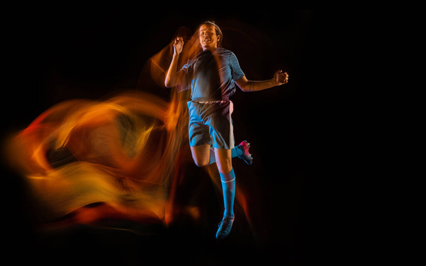 Football or soccer player on black background in mixed light, fire shadows - Foto, imagen