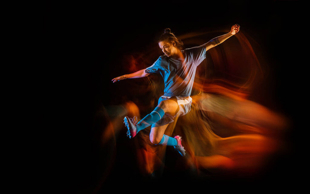 Football or soccer player on black background in mixed light, fire shadows - Fotó, kép