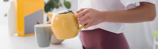 cropped view of young housewife pouring tea into cup, website header - Foto, afbeelding