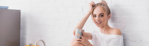 panoramic shot of blonde woman holding cup and looking at camera - Foto, Imagen