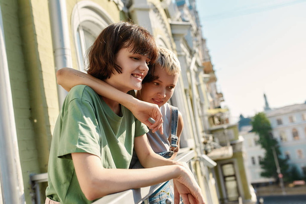 Portrait of young girl looking down, smiling while standing on the balcony with her girlfriend. Lesbian couple spending their day together - Foto, Imagen