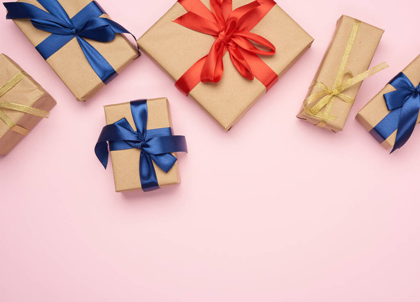 подарочные коробки, завернутые в коричневую бумагу и завязанные красным и синим бантом, подарки на розовом фоне, место для текста - Фото, изображение