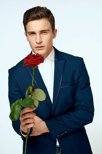 Een man in een pak met een roos in zijn handen een cadeau datum licht achtergrond - Foto, afbeelding