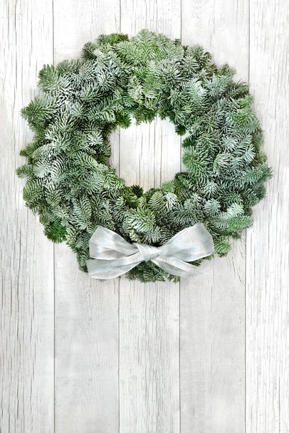Snow covered spruce fir winter wreath with white bow on rustic wood front door background. Composition for solstice, Christmas & New Year. Copy space. - 写真・画像