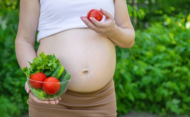 Eine schwangere Frau mit Gemüse in der Hand. Selektiver Fokus. Lebensmittel. - Foto, Bild