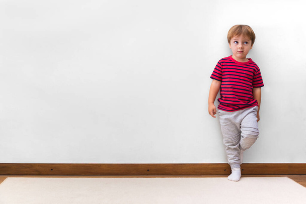Boy with a rogue face and leaning against the wall. White background. Little child in his home. Copy space. - Photo, Image