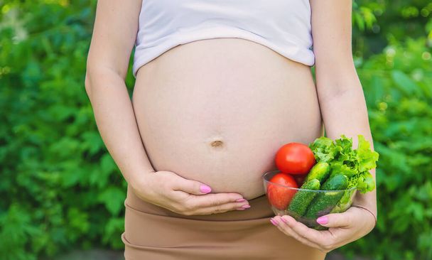 Una mujer embarazada con verduras en las manos. Enfoque selectivo. alimentos. - Foto, imagen