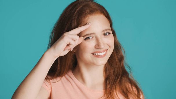 Attractive smiling redhead girl happily showing see you later gesture on camera over colorful background - Photo, Image