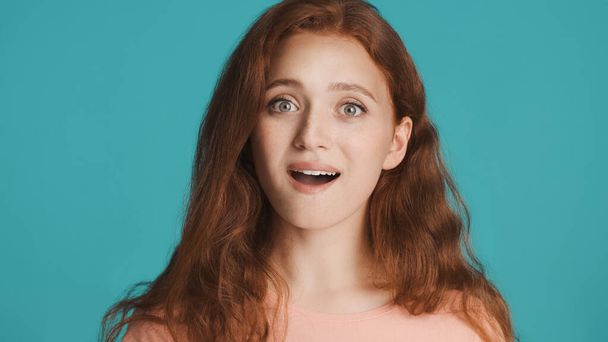 Attractive excited redhead girl amazedly looking in camera over colorful background. Wow expression - Photo, Image